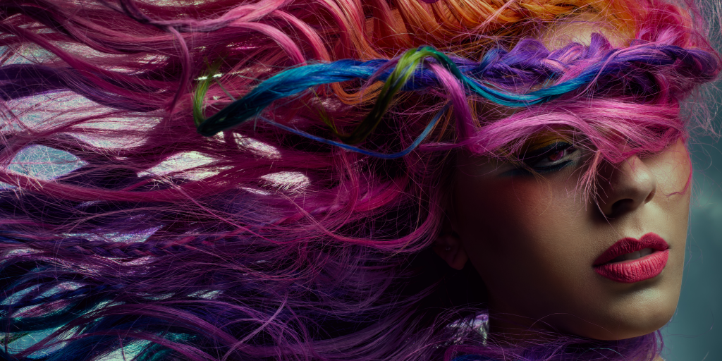 Close-up of a person with vibrant multicolored hair, including shades of pink, purple, and blue, partially covering their face.