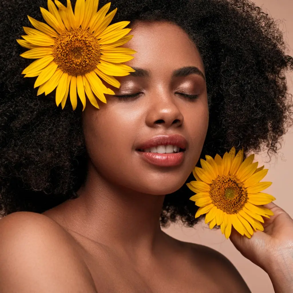 Curly-haired woman with sunflowers in hand and hair, eyes closed